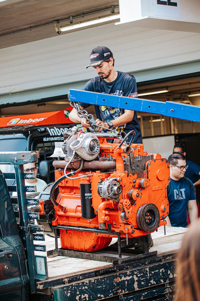Skilled mechanic working on a large orange engine with a hoist, outdoors in São Paulo.