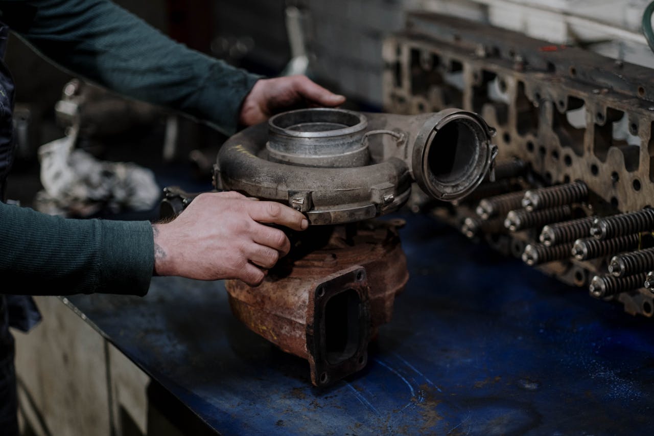 Mechanic's hands repairing a turbocharger in a workshop setting.