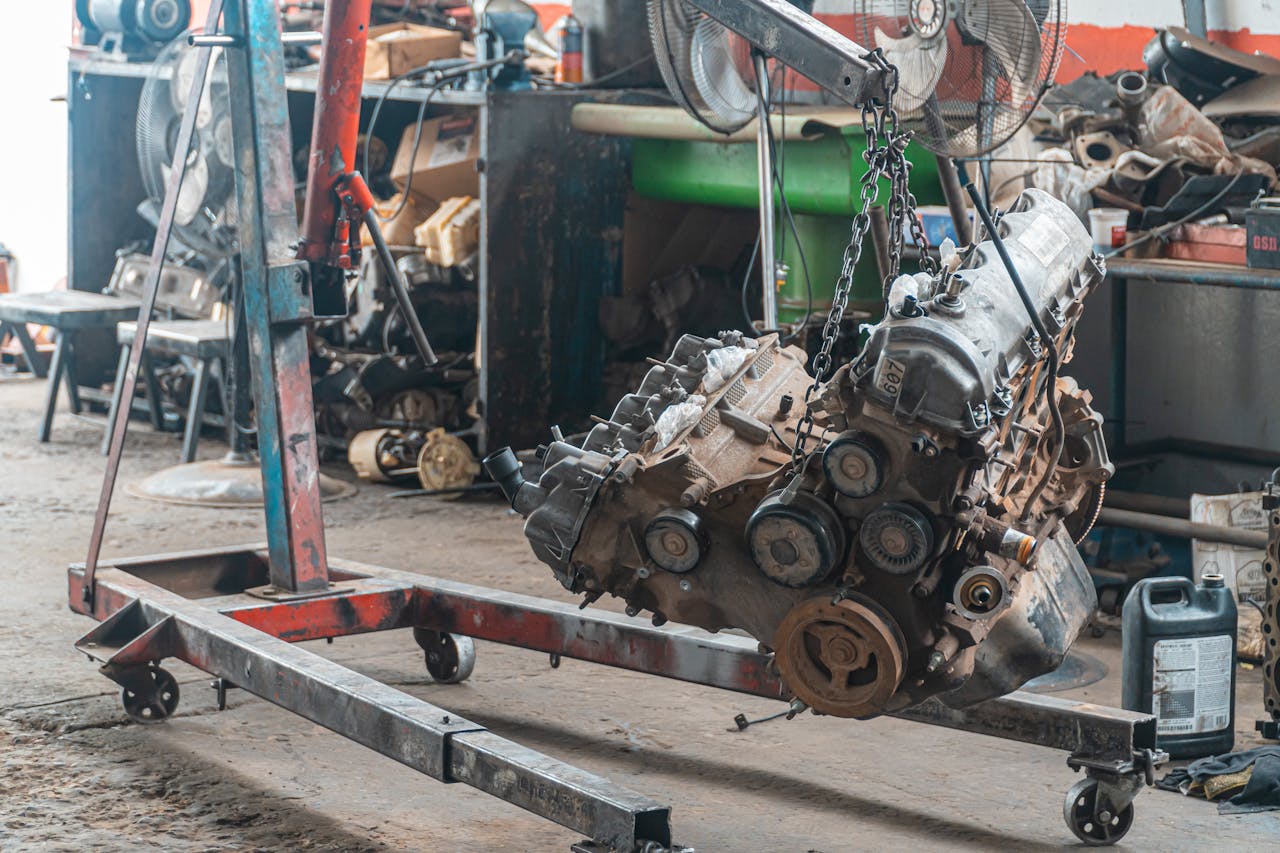 Close-up of a car engine hoisted in a mechanic's workshop, showcasing industrial tools.